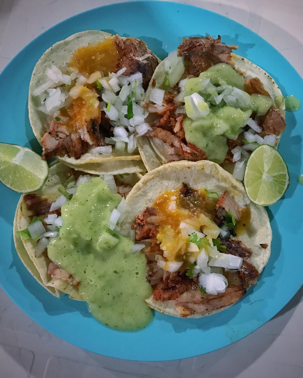Vier Al-Pastor-Tacos mit Salsas, Zwiebeln und Limette auf blauem Teller